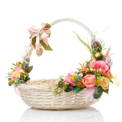 Fototapeta na wymiar A very nice round white Easter basket with a bow on the handle and a variety of flowers. Decor in delicate pink and green colors.