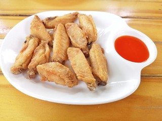 Fried chicken wings, placed in a white container There is a red tomato sauce, the wood floor is the background.