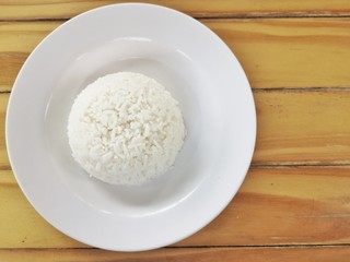 White steamed rice Placed into a sphere In a white plate With a wooden floor as the background.