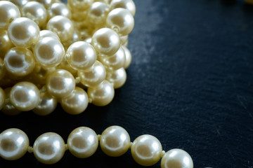 Pearl necklace on a black slate plate, a hoof of shiny pearls behind, copyspace, selective Focus