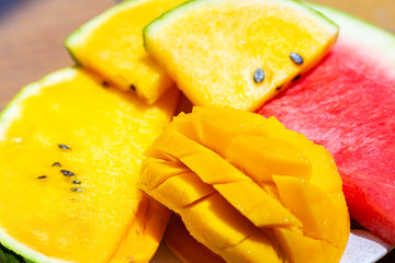 Closeup ripe juicy sliced fruits of mango and red and yellow watermelon. Sweet and colorful fruit plate