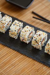 Uramaki served on a black slate with wooden black sticks and soy sauce. Japanese traditional food with bamboo service.