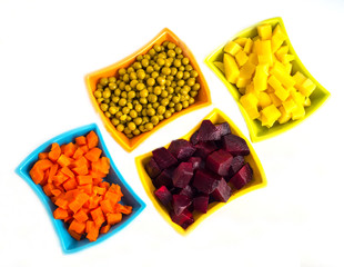 Potatoes, carrots, red beets, peas cut into cubes and folded into plates on a white background