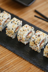 Japanese sushi rolls sprinkled with sesame seeds on a black stone board.