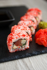 Sushi roll with seafood and soy sauce, wasabi and ginger. Sushi roll on a black board.