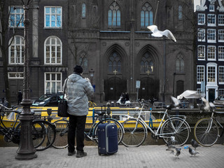 Obraz premium Imagen callejera de Amsterdam cerca de un canal y un viajero mirando las palomas entre las bicicletas