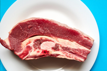 Raw veal steak on a white plate on a blue background.