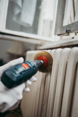 Beautiful and diligent middle age handy woman renovating her old home or apartment. She is holding professional grinder and brushing radiator for later painting. Do it yourself housework concept.