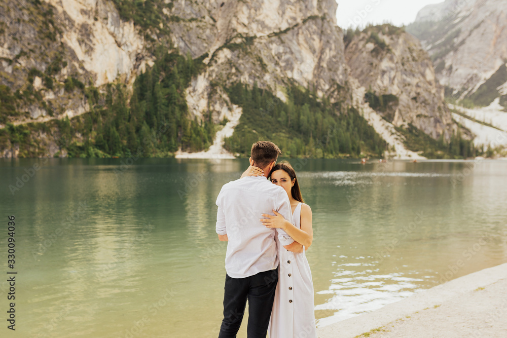 Wall mural girl looks out behind guy's shoulder. loving couple on lake background. a couple embrace on the shor