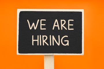 We are Hiring written on a chalkboard against orange background - Business Concept