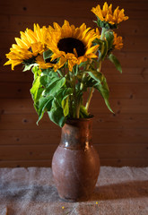 A bouquet of sunflowers in a vintage ceramic jug stands on a table covered with a rough cloth on a wooden background.