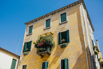 Fototapeta na wymiar Venetian architecture. An ancient building in the Venetian style of architecture. Red flowers and green plants on vintage building in Venice, Italy. Ancient balcony. 