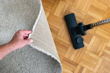 Vacuum cleaner extension on a laminated wooden floor close to a grey fabric rug held up by male...