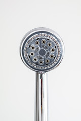 Silver round shower head with hard water deposits all around the sprinklers isolated against light...