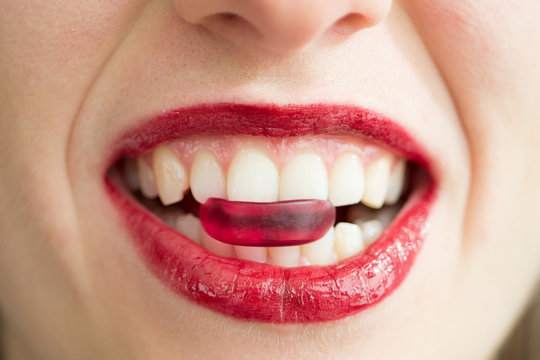 Young Caucasian woman biting into red candy sweet mouth open