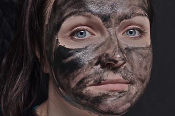 Woman with a black mud mask or clay on her face on a black background. Close-up.