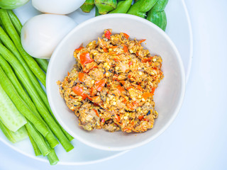 Top view or directly above and closeup of Thai chili sauce (Nam Prik) in the ceramic bowl with boiled eggs and vegatables on ceramic dish and gray background.