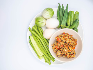 Top view or directly above of Thai chili sauce (Nam Prik) in the ceramic bowl with boiled eggs and vegatables in ceramic dish and gray background.