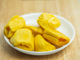 Closeup of yellow ripe jackfruit on white ceramic dish and wooden table in the kitchen or restaurant.