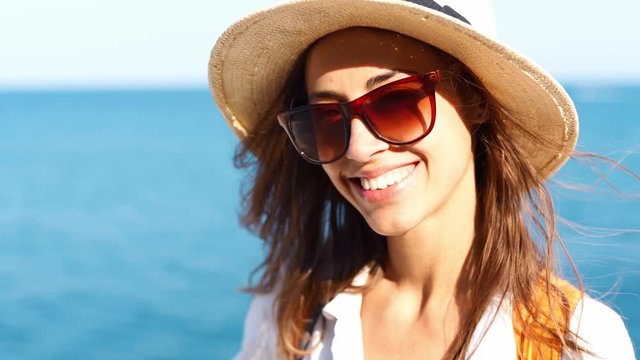 closeup charming smiling woman traveler in straw hat and sunglasses walking at seaside at sunny day on blue sea background. luxury resort carefree tourism destination female sunhat