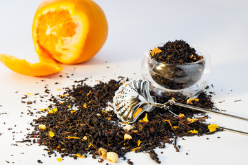 Dry tea herbs with orange, glass cup and tea strainer on white background.