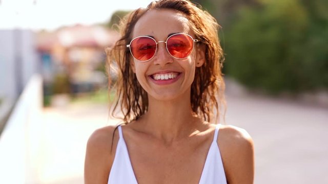 slow motion close up portrait of Beautiful young tanned woman in pink sunglasses posing on bay at seaside on resort and joyfully smiling. wind flying hair