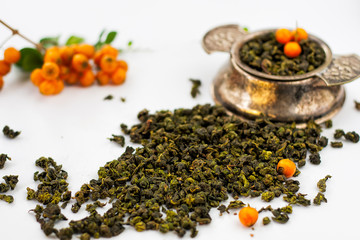 Dry tea herbs with orange berries and vintage silver tea strainer on white background.