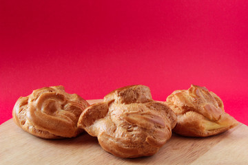 Homemade profiteroles with custard, eclairs. On a wooden board, with a red background. French dessert.