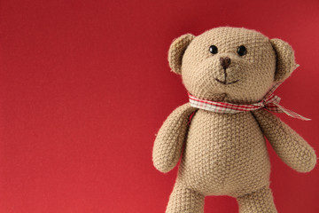 Brown teddy bear, toy is standing on a red background, close up.
