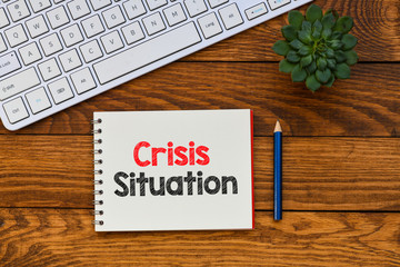 Crisis situation text written in notebook on a wooden table.