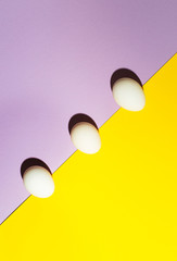 White easter egg on a lilac and yellow background on bright light, flat lay, copy text. Minimal concept