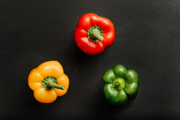 composition with sweet pepper of different colors on a rough black surface.