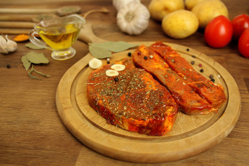 raw meat, two meat pickled in spices meat medallions on a round wooden board on the table, garlic, bay leaf, potatoes and tomatoes nearby, cooking concept, copy space