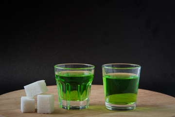 Strong alcohol. two shot glasses with absinthe, white sugar. on a black background