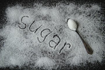 the word sugar on a black background, written diagonally, with a spoon of sugar