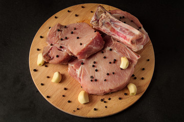 meat, raw steaks with garlic and pepper on a wooden board, black background