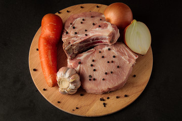 raw meat, steaks, carrots, garlic and onions cut in two, on a wooden board