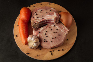 two steaks, raw meat, with vegetables, onions garlic, carrots and peppers, on a wooden board