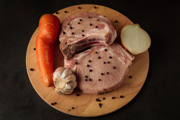 raw meat, steaks with carrots, chopped onions, garlic and pepper, on a wooden board