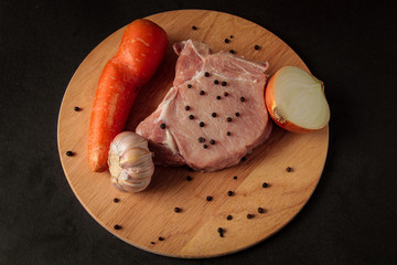 one raw meat steak, on a wooden board, sprinkled with pepper, with vegetables, onions, garlic, carrots