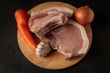 Meat. Raw pieces of pork, with vegetables, garlic, onions, carrots, on a wooden board