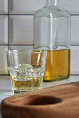 Gold tequila in a glass with ice cubes on the background of a cutting Board and a bottle of tequila. Vertical.