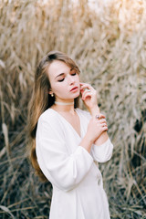 portrait of a young attractive girl in a light white dress and black shoes standing among the reeds in autumn