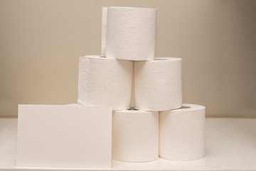 Toilet paper rolls pile on neutral background and white card for text input. Shortage and stockpile concept