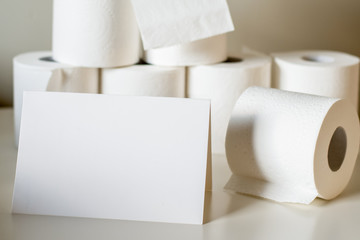 Toilet paper rolls pile on neutral background and white card for text input. Shortage and stockpile concept