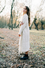 portrait of a young attractive fair haired girl in a light white dress and black shoes among a picturesque forest in autumn