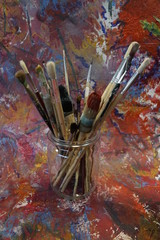 old brushes in a glas in front of colorful paper