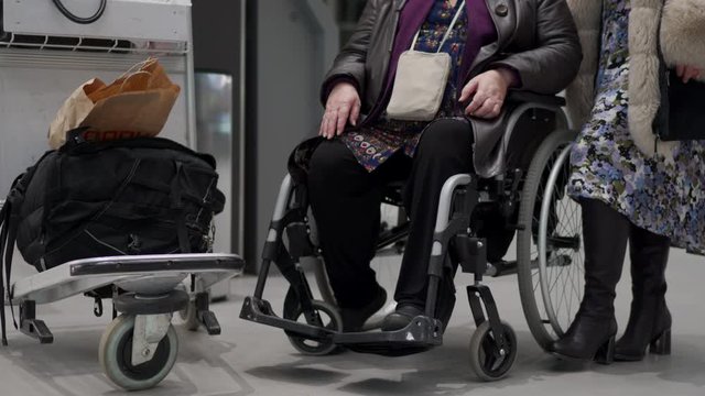 Wheelchair service in airport terminal, disabled person sitting in wheelchair, elderly woman with a family waiting for departure.