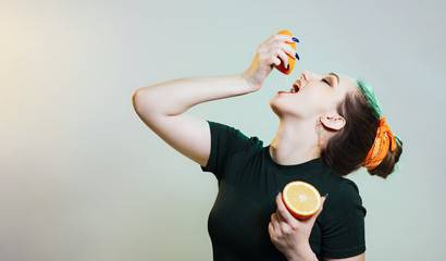 beautiful stylish girl threw head back and squeezes a drop of juice from half an orange into her mouth, a woman drinks fruit juice, a healthy diet concept