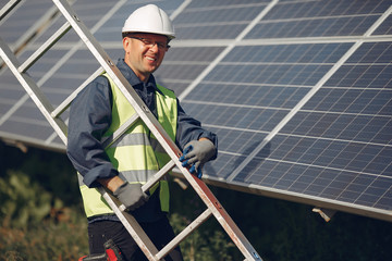 Engineer in a white helmet. Man near solar panel. Worker with a ladder